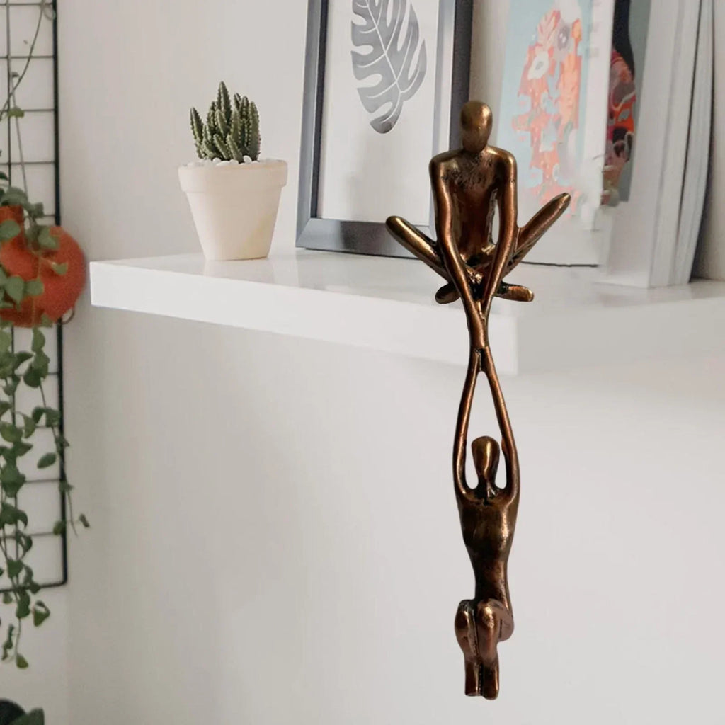 Skulptur i to dele, hvor den ene figur sidder på hyldekanten og holder den anden, bronze eller sort