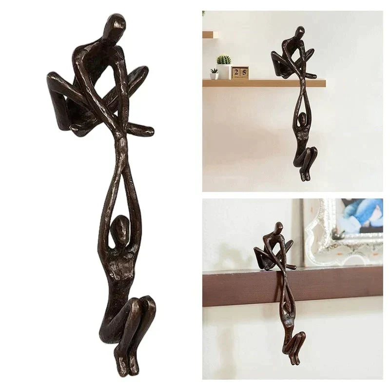 Skulptur i to dele, hvor den ene figur sidder på hyldekanten og holder den anden, bronze eller sort