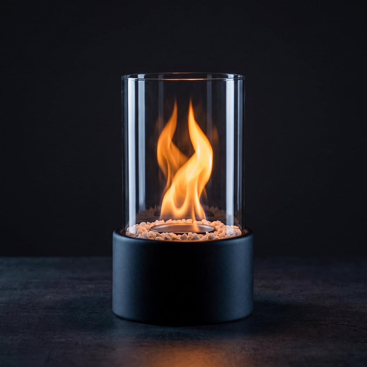 Tændt bioethanolpejs i glas med flamme over stenene i den sorte bund