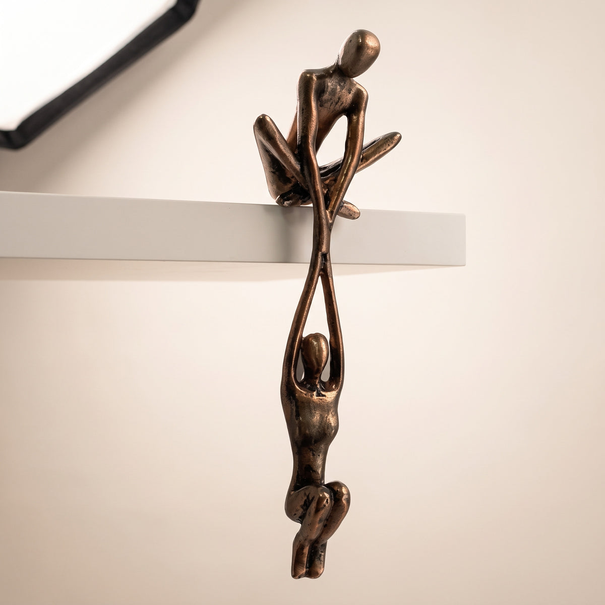Bronzeskulptur med to figurer, den ene sidder på hyldekanten og holder den anden hængende