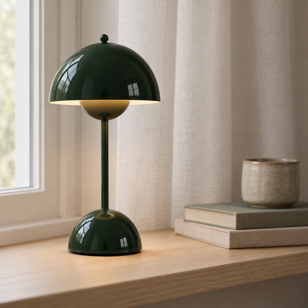 Bordlampe uden ledning i mørkegrøn, tændt på en vindueskarm i lys eg